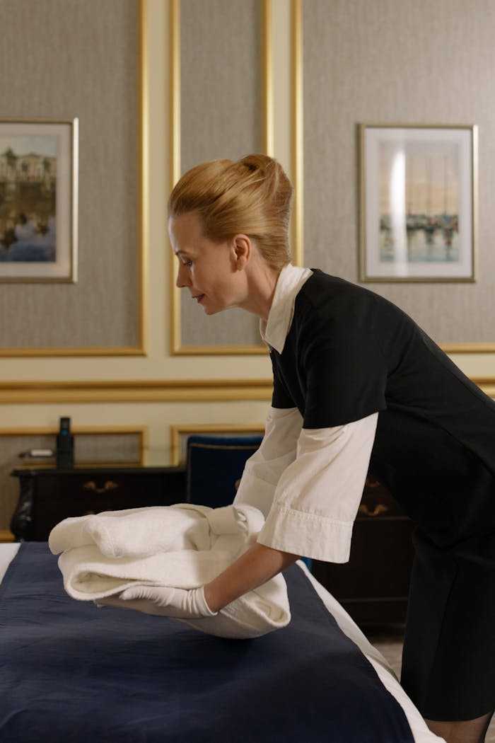 Elegantly dressed housekeeper in a hotel room arranging clean linens on the bed.